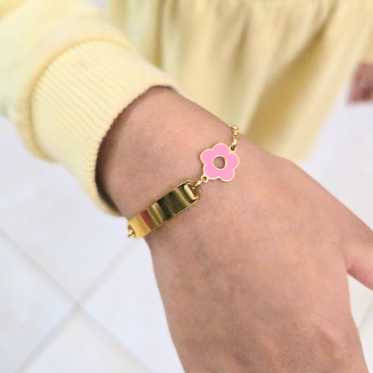 Gold bracelet with a pink flower charm on a wrist against a light background