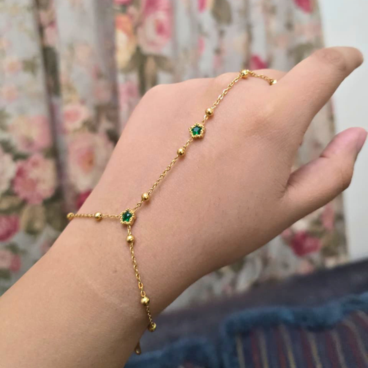 Gold bracelet with green gemstones on a wrist against a floral background