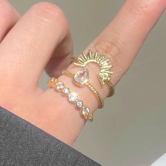 Close-up of a hand wearing multiple gold and rose gold rings with gemstones on a neutral background.