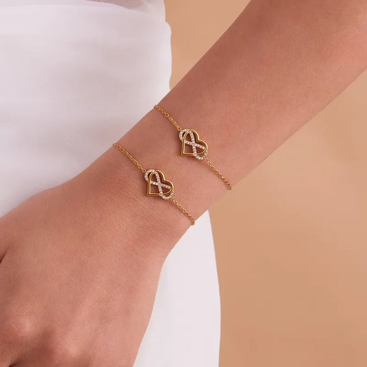 Gold bracelet with heart-shaped charms on a wrist against a neutral background