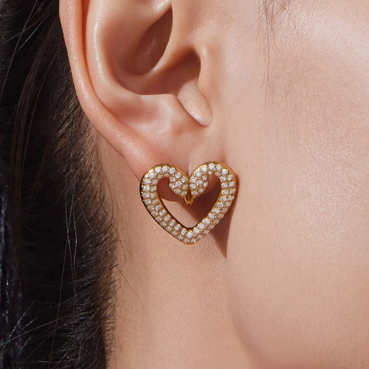 Close-up of an ear wearing a gold heart-shaped earring with pearls.
