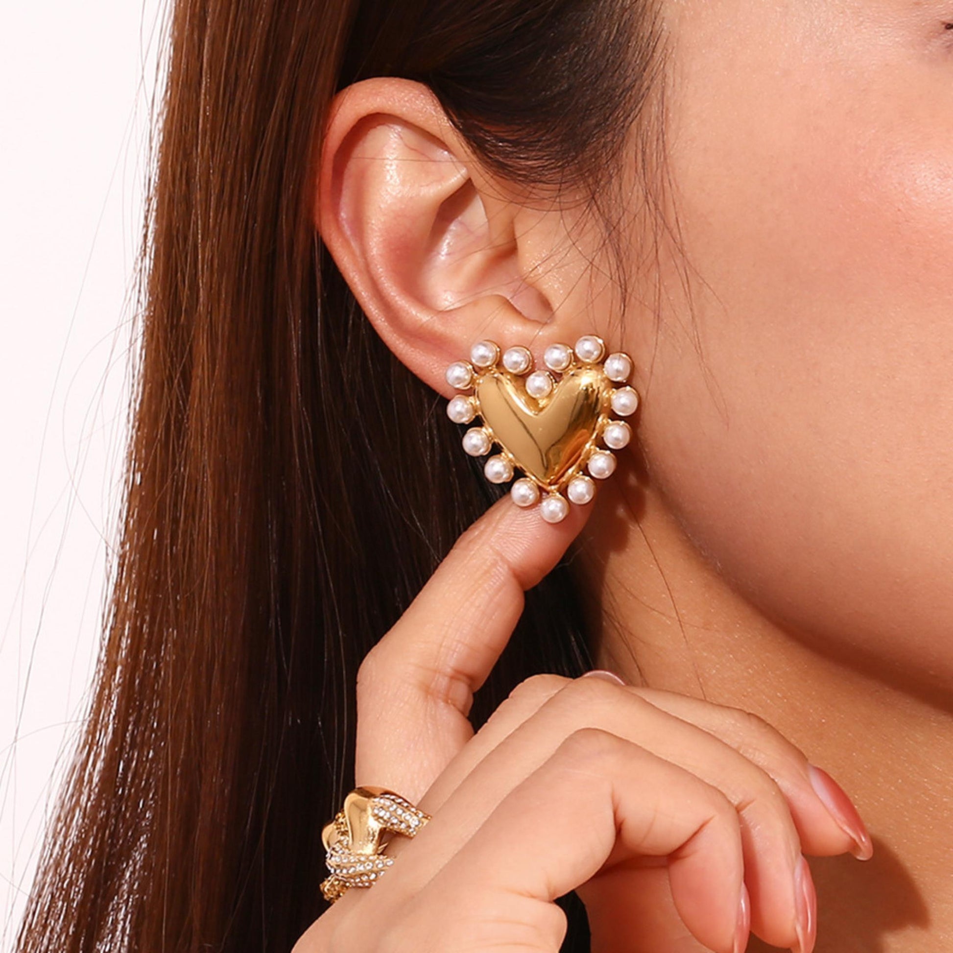 Heart-shaped gold earring with pearls worn by a person