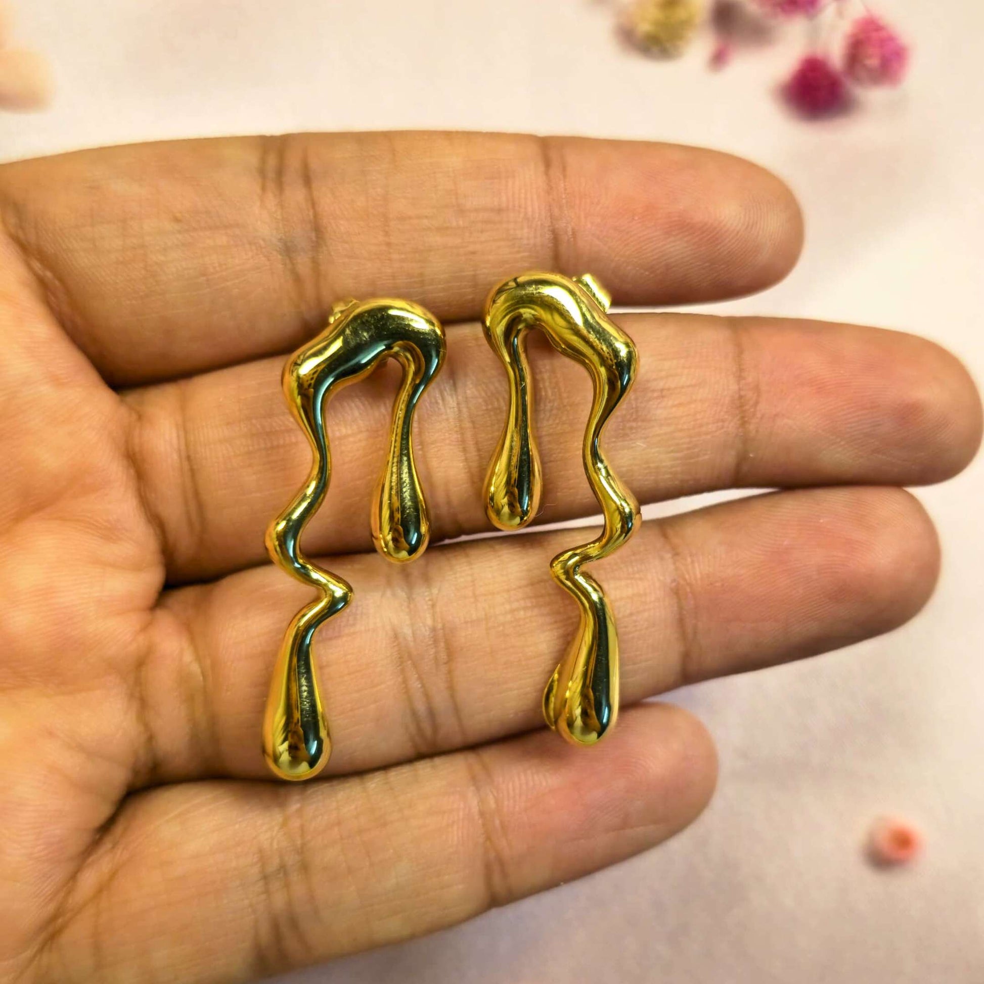 Gold geometric earrings held between fingers against a neutral background