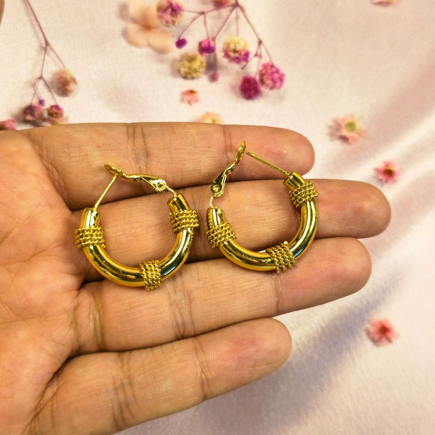 Gold hoop earrings held in a hand with a soft floral background