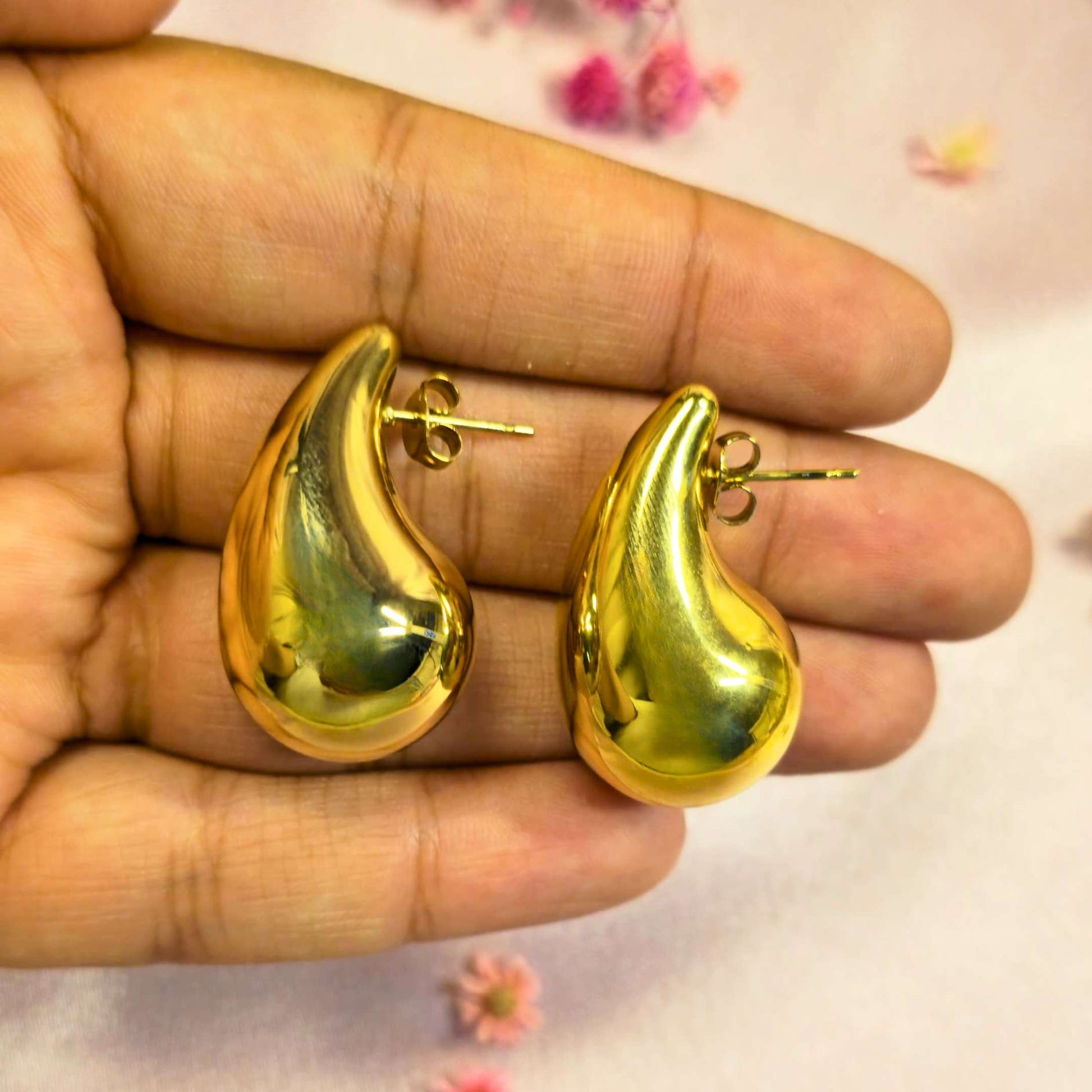 Gold teardrop-shaped earrings held in a hand with a light background
