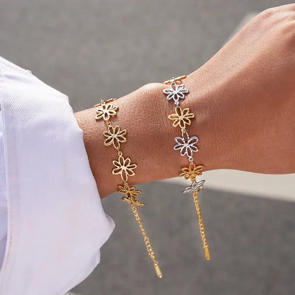 Gold and silver flower-shaped bracelets on a wrist against a neutral background