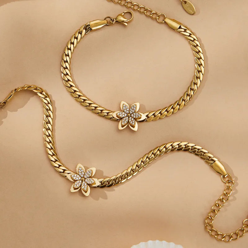 Gold chain bracelet with floral clasp on a beige background