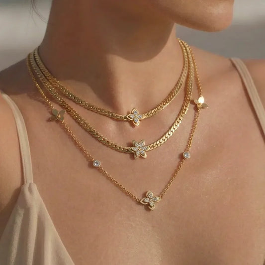 Gold necklaces with floral pendants on a person wearing a beige top.