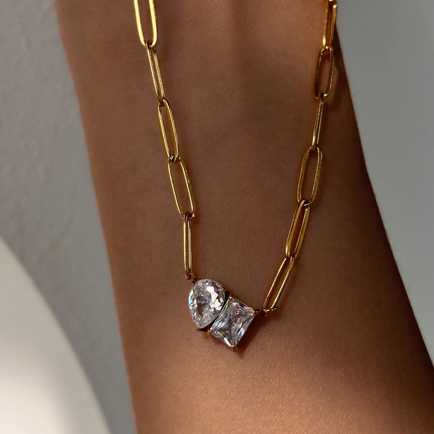 Gold chain necklace with heart-shaped crystals on a person's wrist against a neutral background
