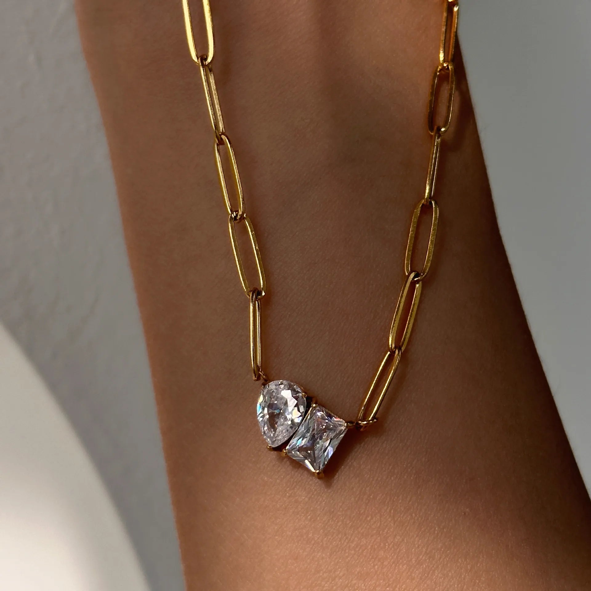 Gold chain necklace with heart-shaped crystals on a person's wrist against a neutral background