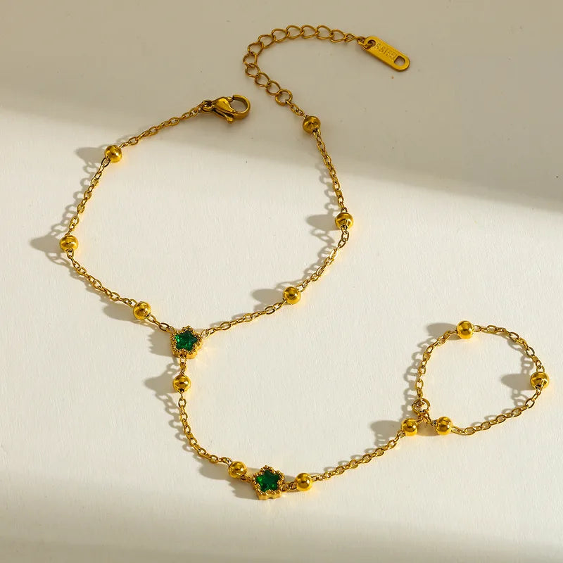 Gold handchain with green gemstones on a light background