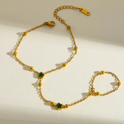 Gold handchain with green gemstones on a light background