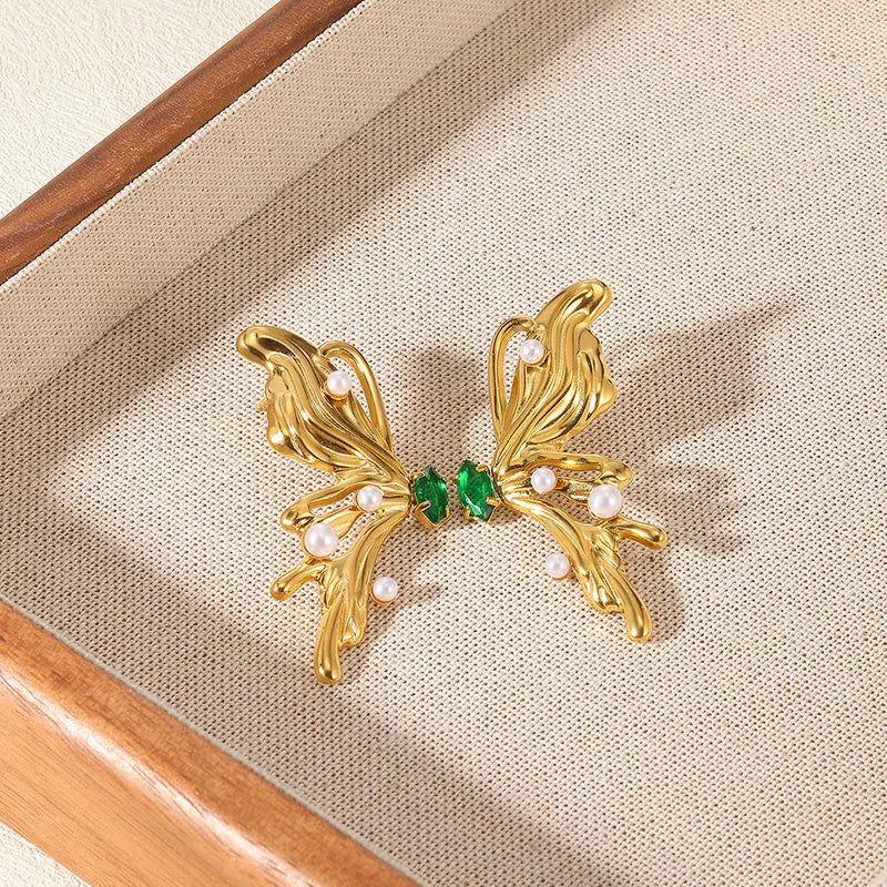 Gold earrings with green and pearl accents on a beige fabric background