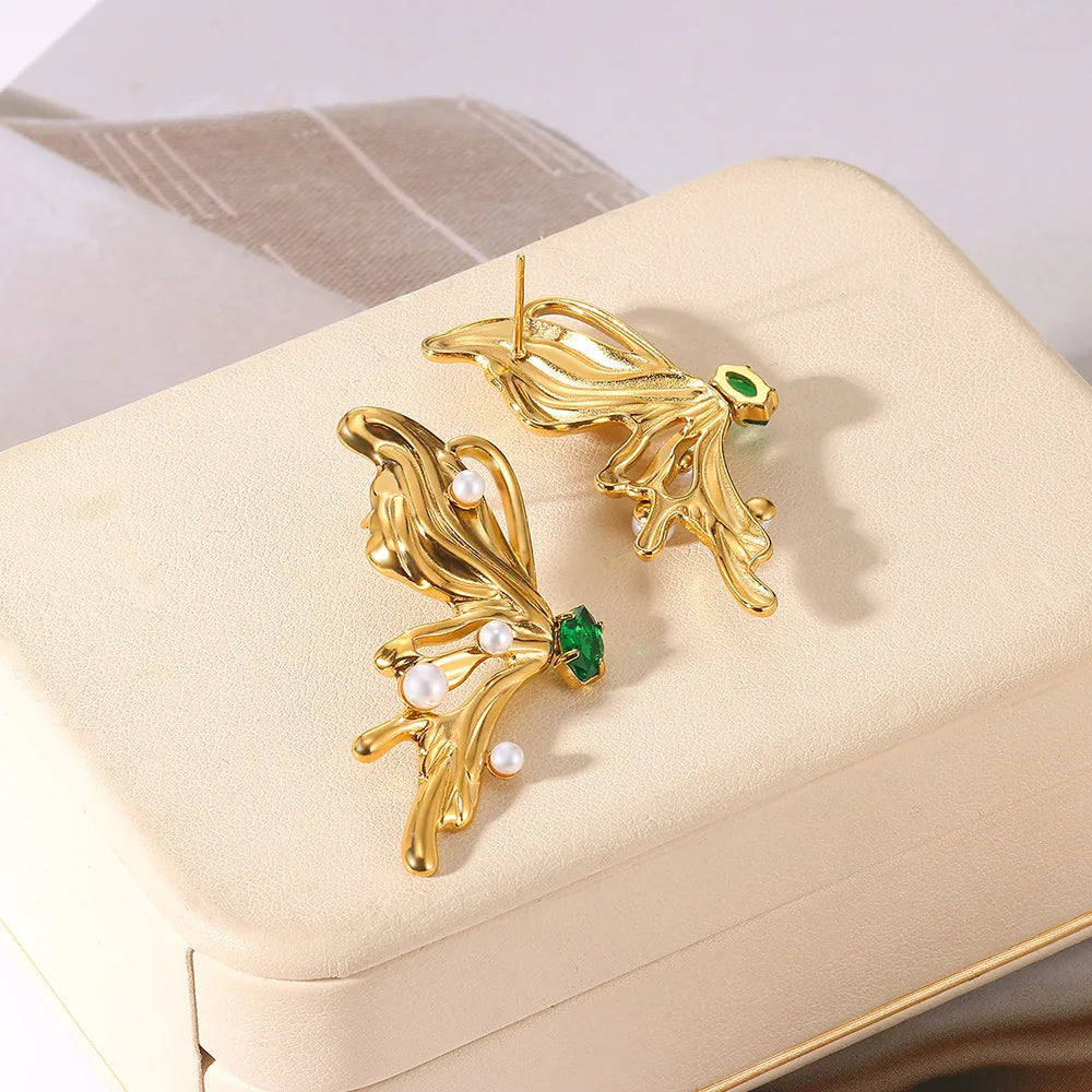 Gold earrings with green gemstones and pearls on a beige jewelry box