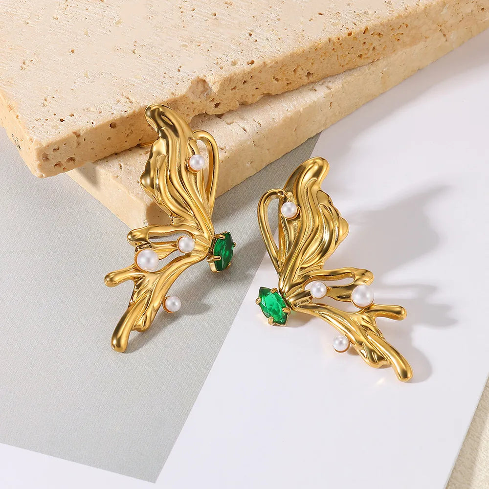 Gold earrings with green gemstones and pearls on a light background