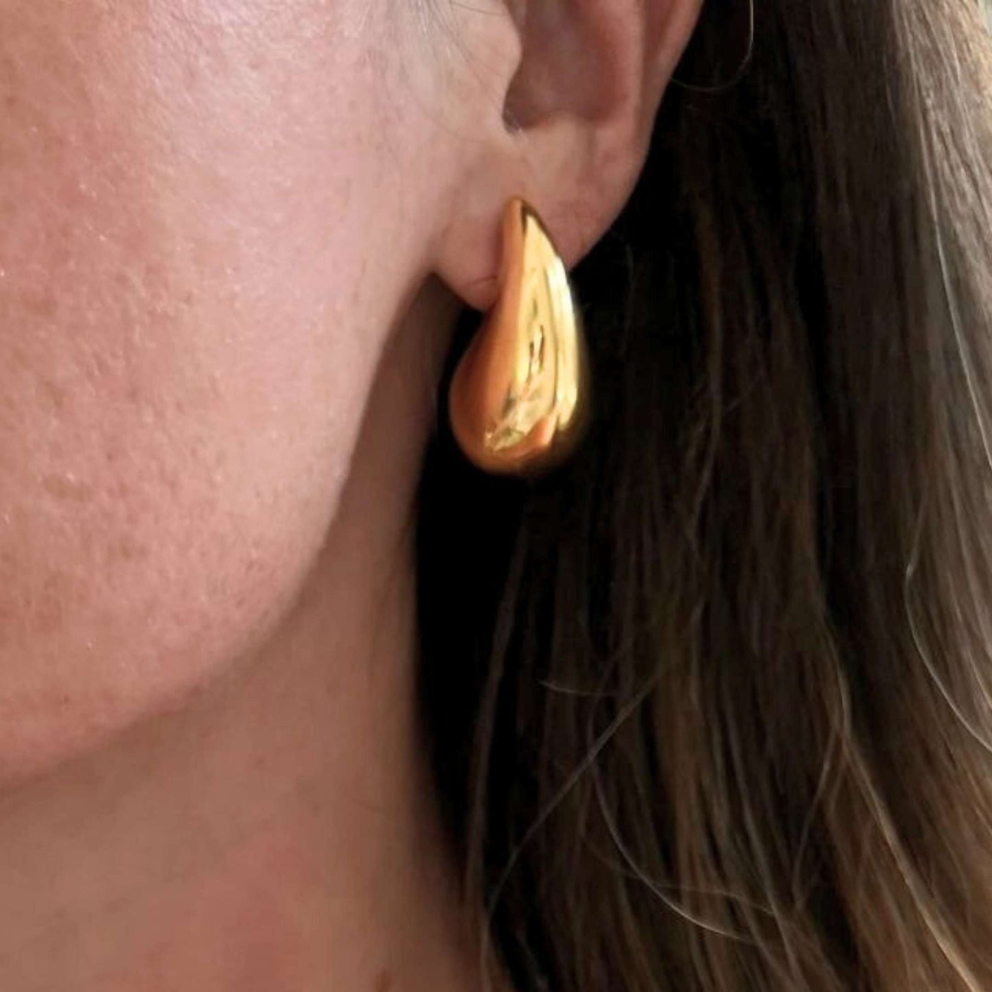 Gold teardrop earring worn by a person with brown hair.