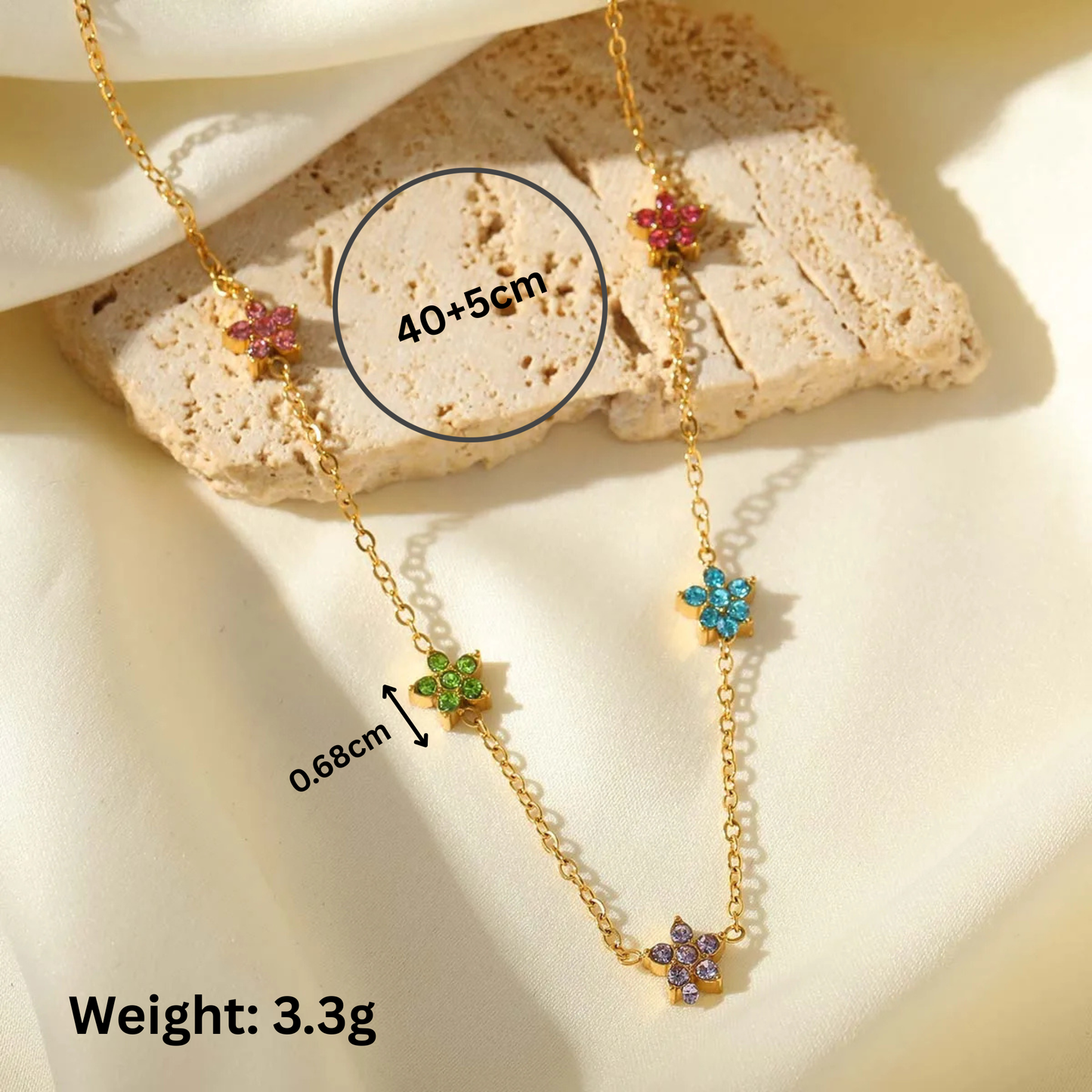 Gold necklace with colorful flower pendants on a stone surface, showing measurements and weight.