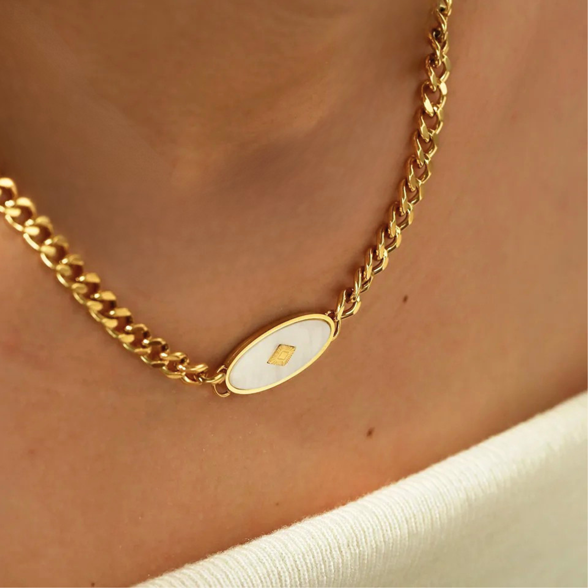 Gold chain necklace with a white pendant on a person's neck