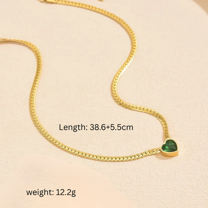 Gold chain necklace with a green heart pendant on a beige background
