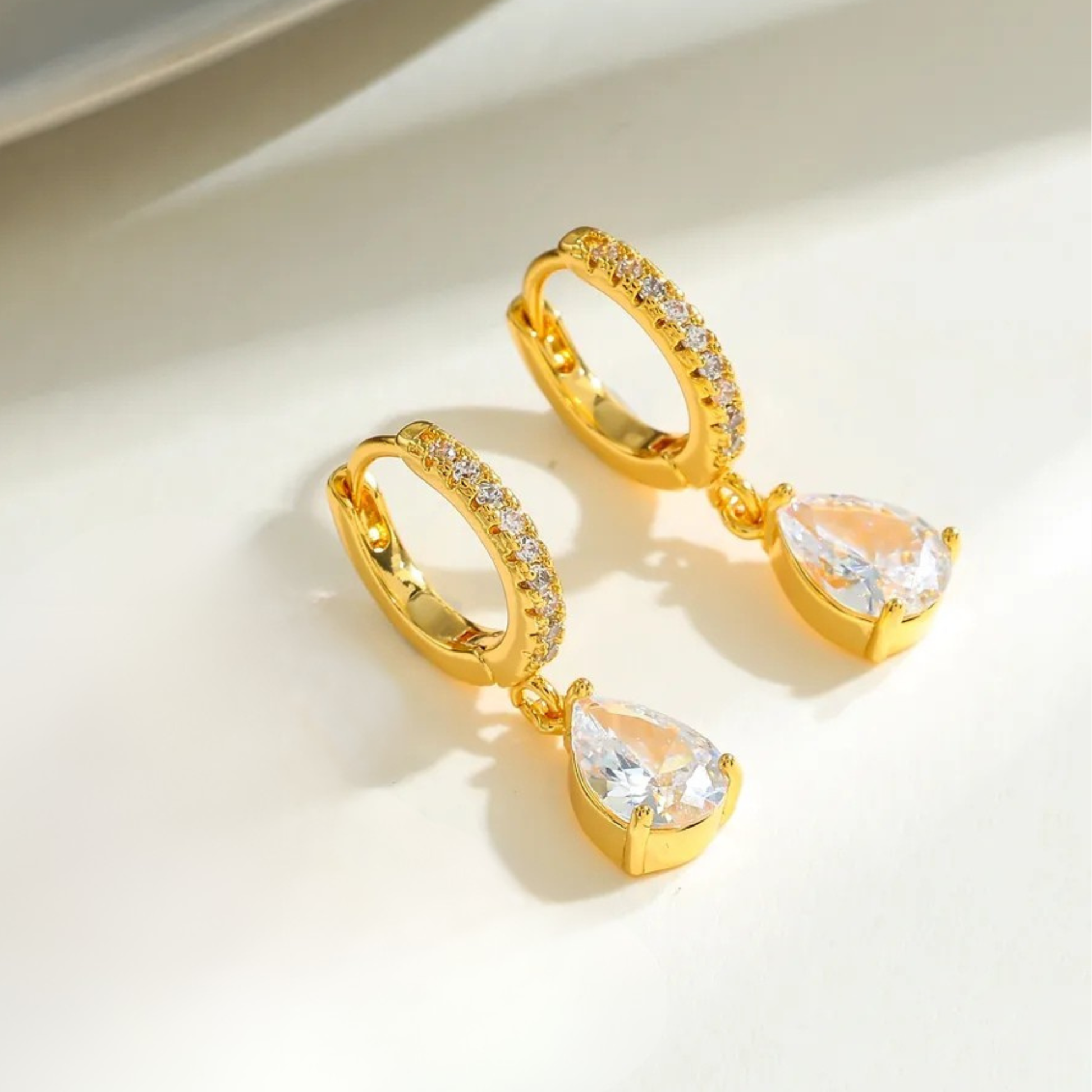 Gold hoop earrings with teardrop-shaped gemstones on a light background