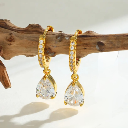 Gold hoop earrings with teardrop-shaped crystals on a wooden branch