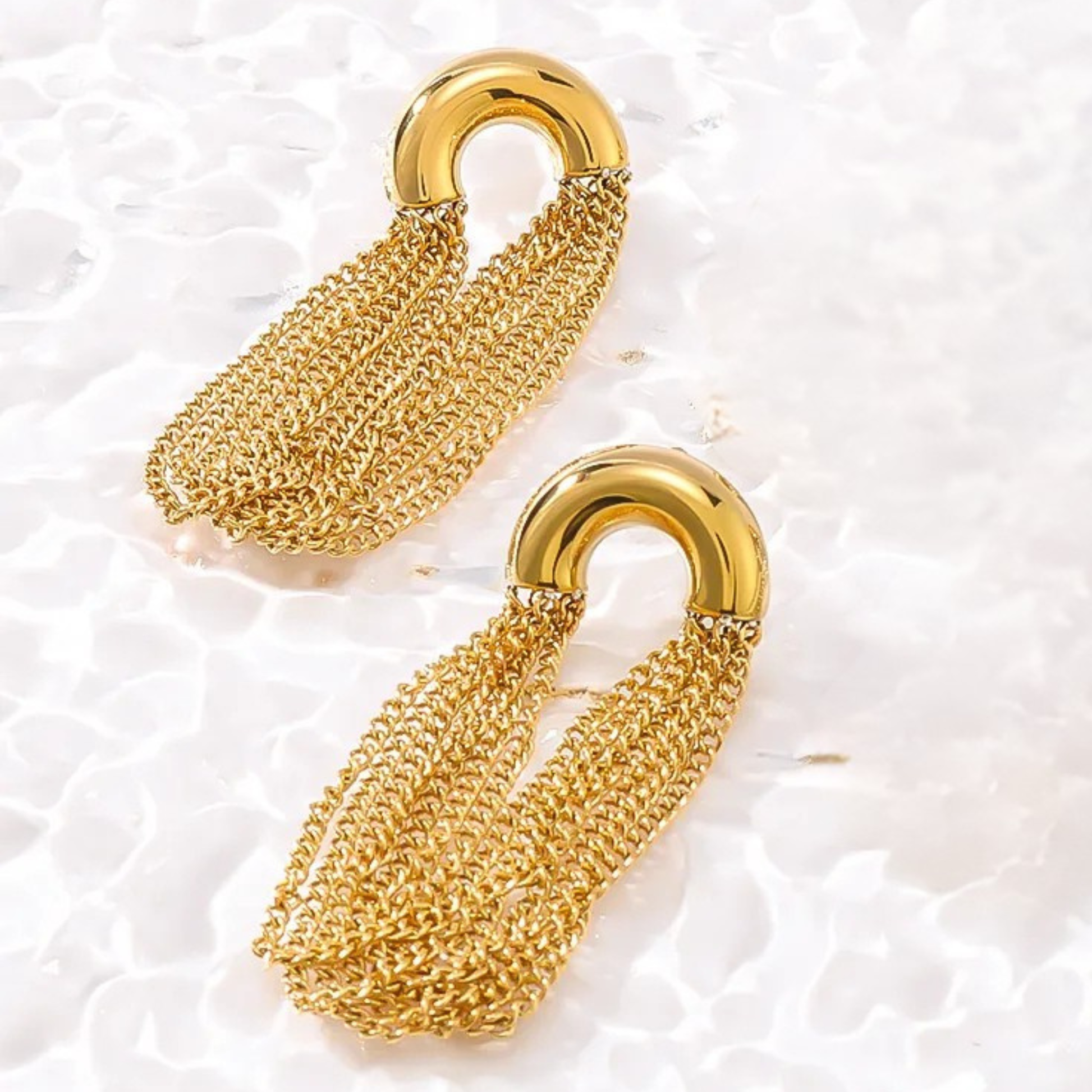 Pair of gold chain earrings on a textured white surface