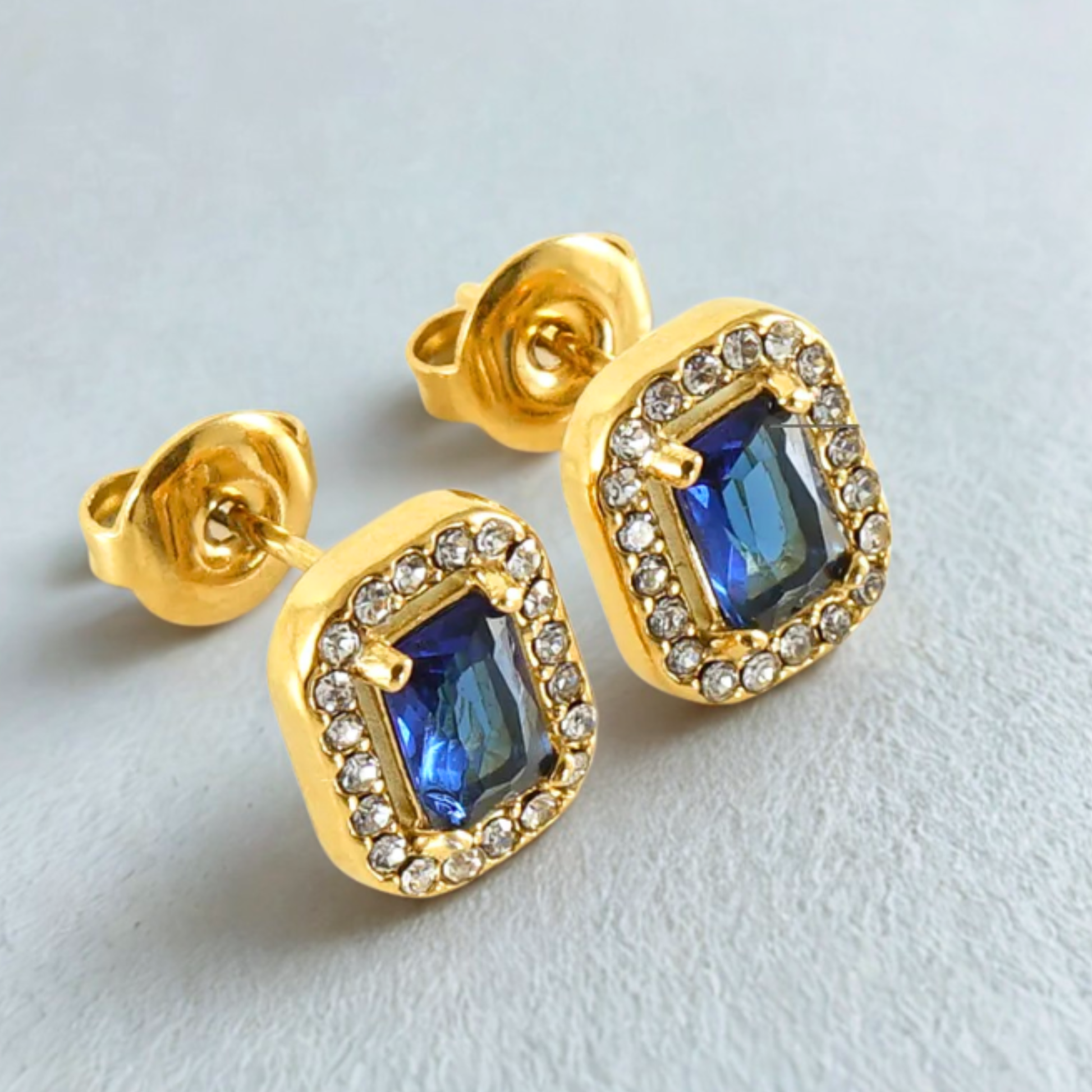 Gold earrings with blue gemstones on a light gray background