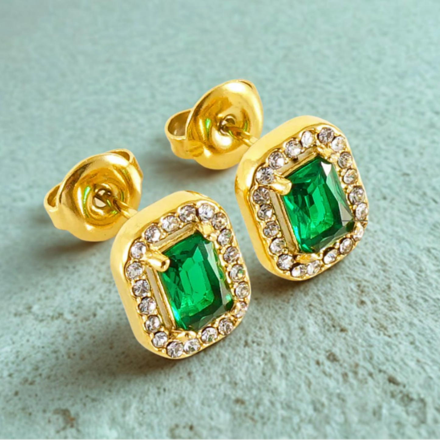 Gold earrings with green gemstones on a light blue background
