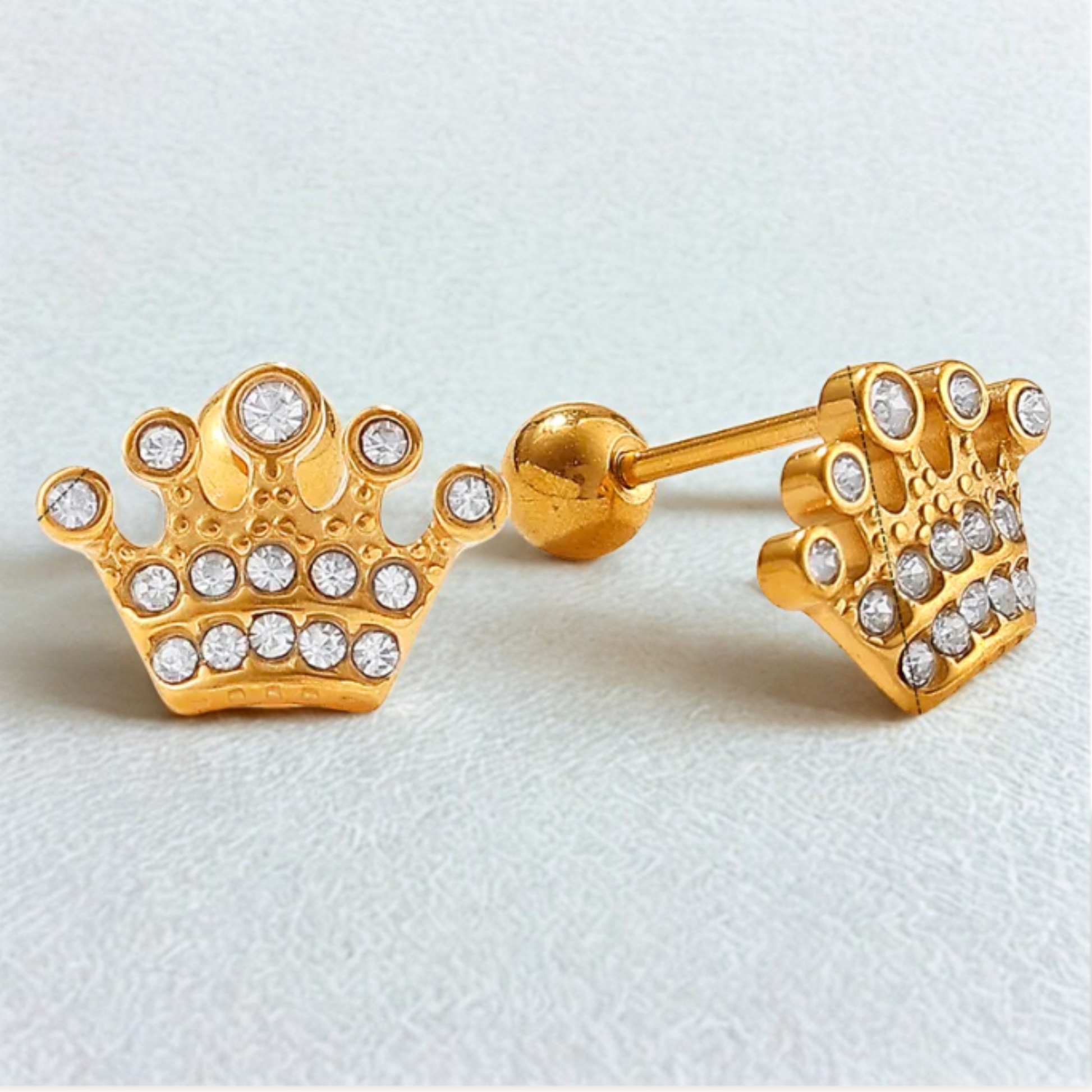Gold crown-shaped earrings with clear stones on a light gray background
