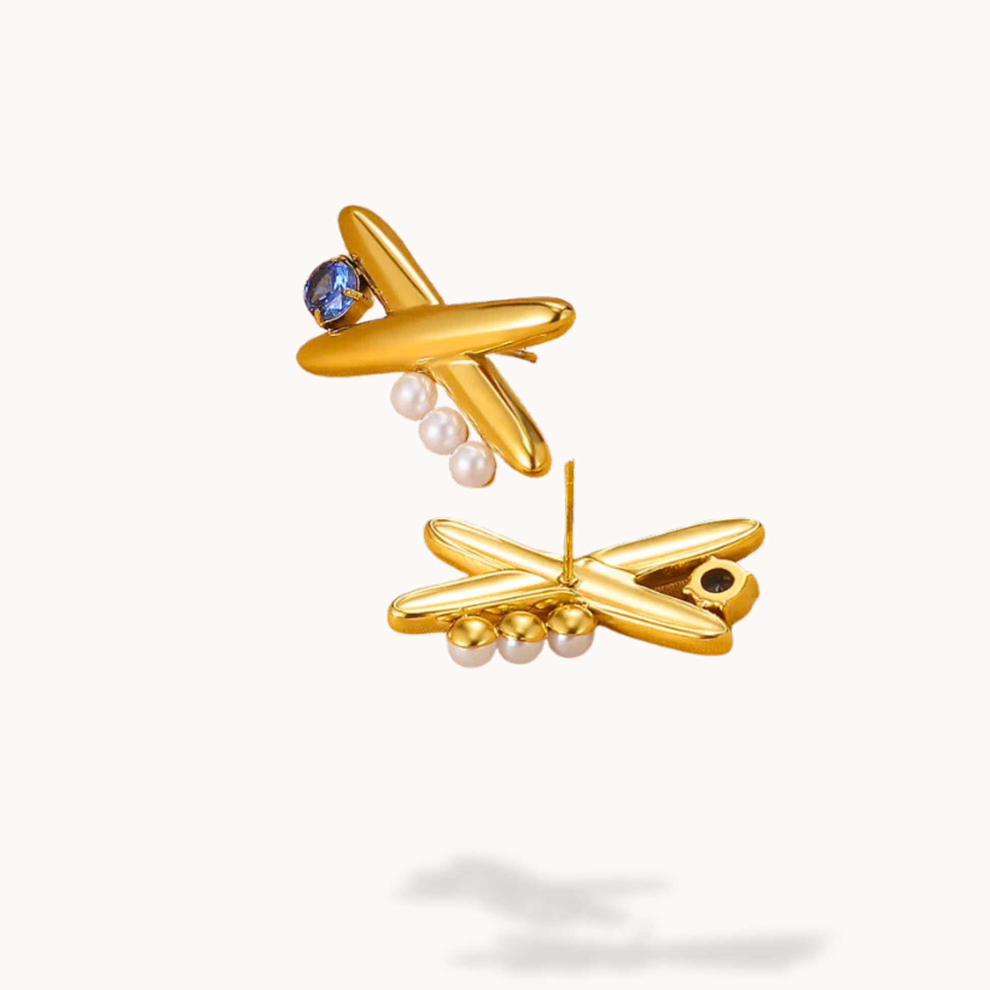 Gold airplane-shaped earrings with pearls and gemstones on a white background