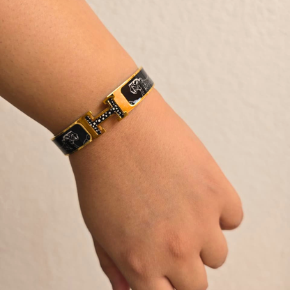Gold and black bracelet on a wrist against a beige background