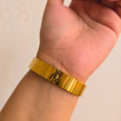 Gold bracelet on a wrist against a neutral background