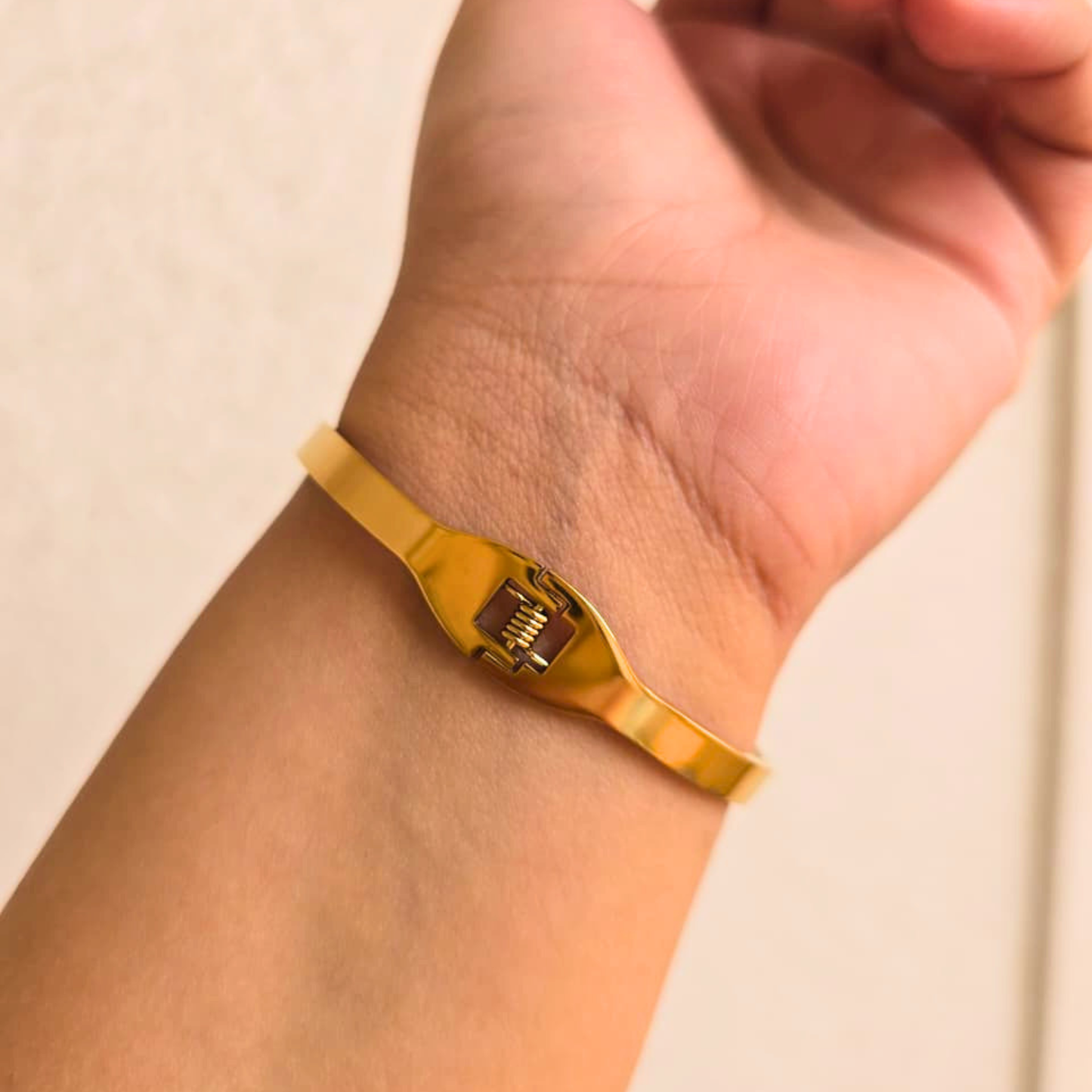 Gold bracelet on a wrist against a beige background