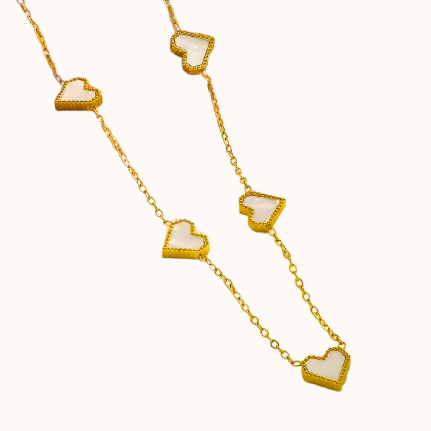 Gold necklace with white heart pendants on a white background