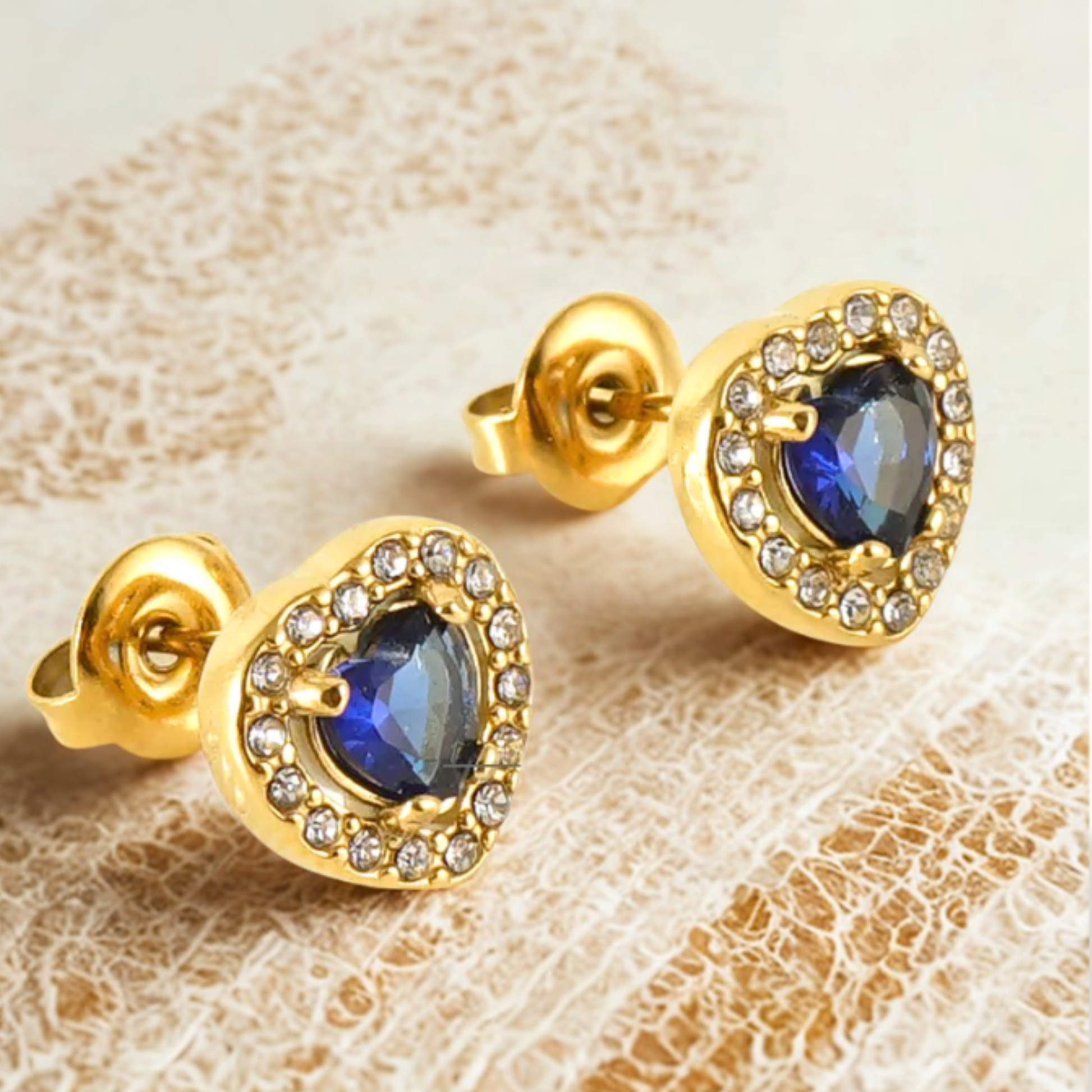 Gold earrings with blue gemstones on a textured beige background