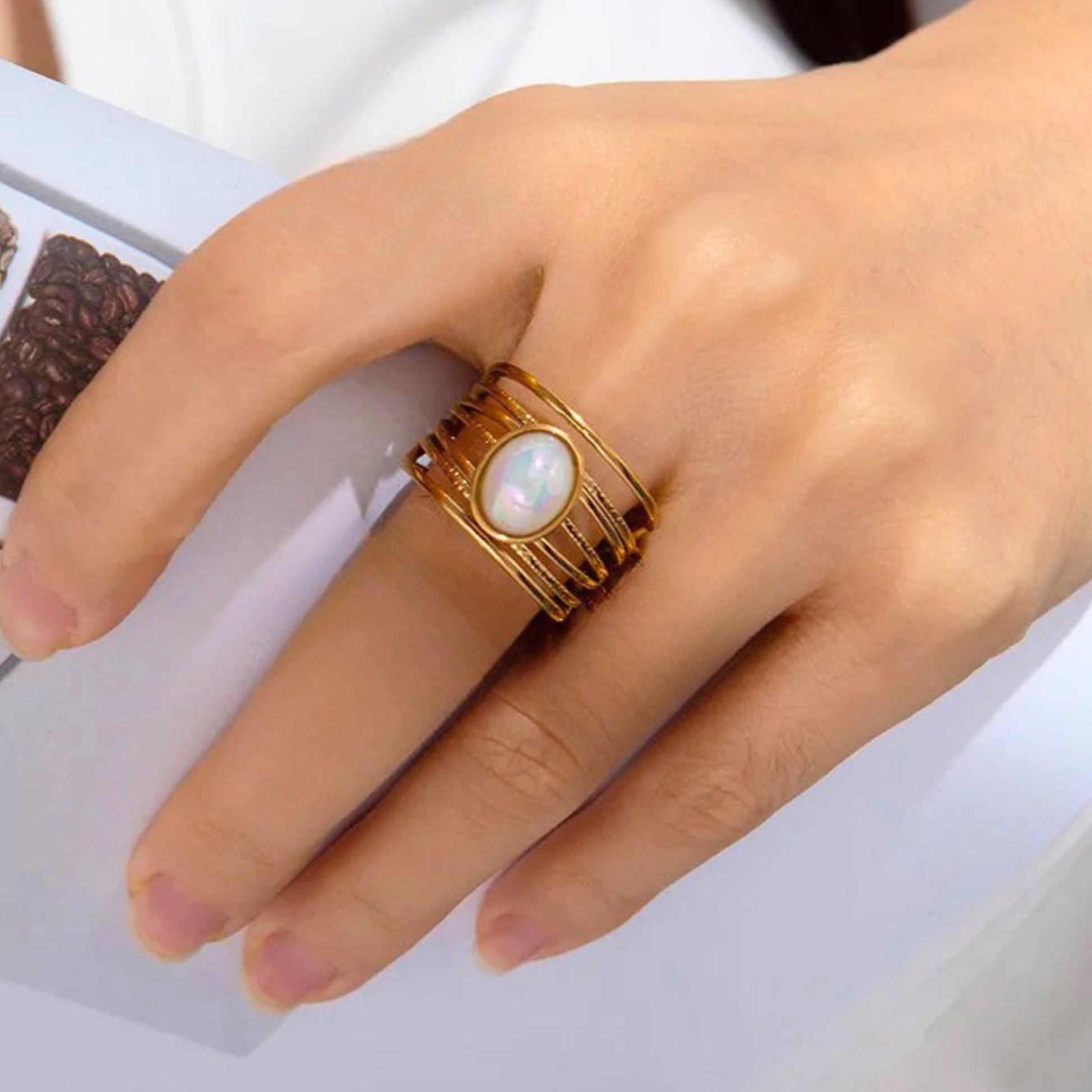 Gold ring with a central pearl on a hand against a white background