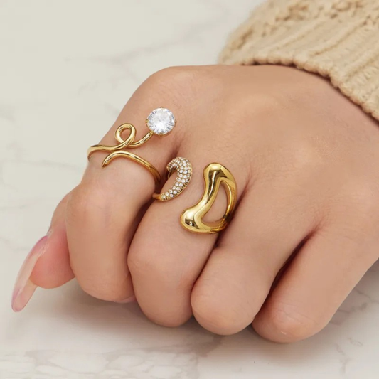 Hand wearing multiple gold rings with different designs on a neutral background