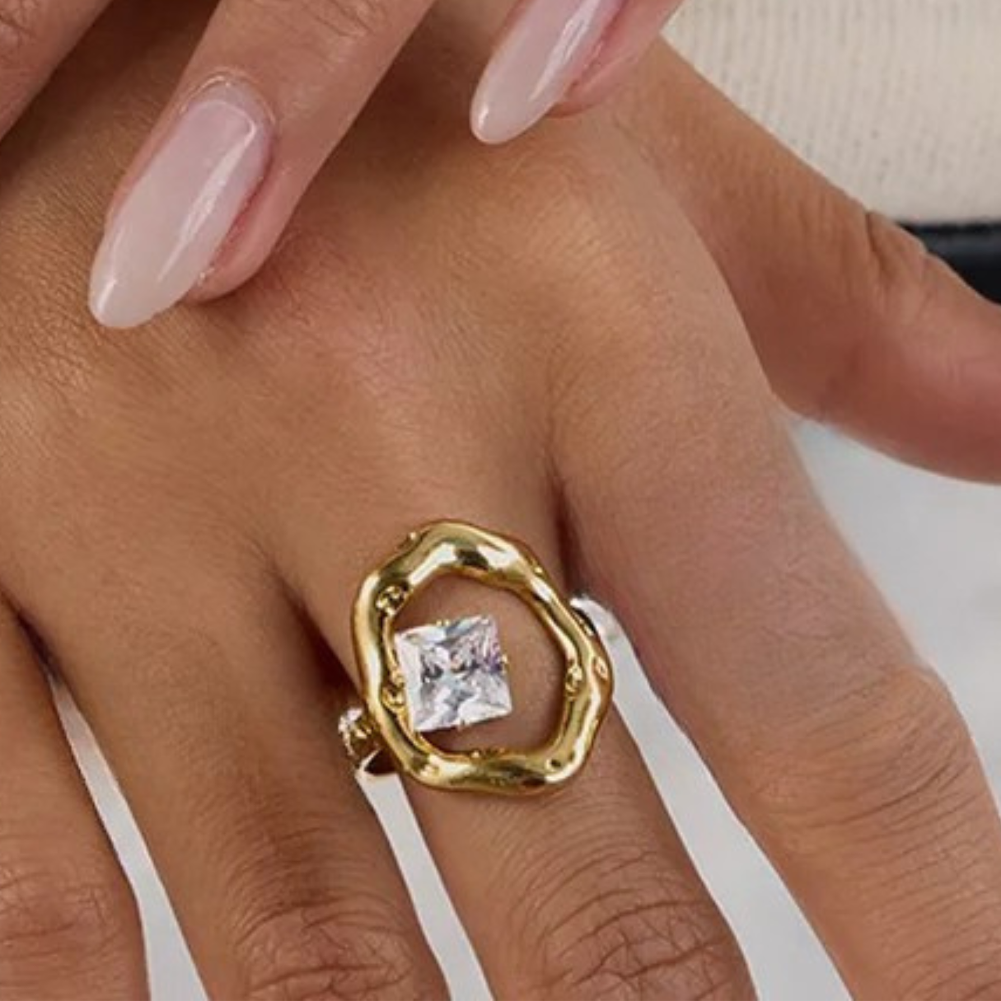 Gold ring with a diamond on a hand against a neutral background