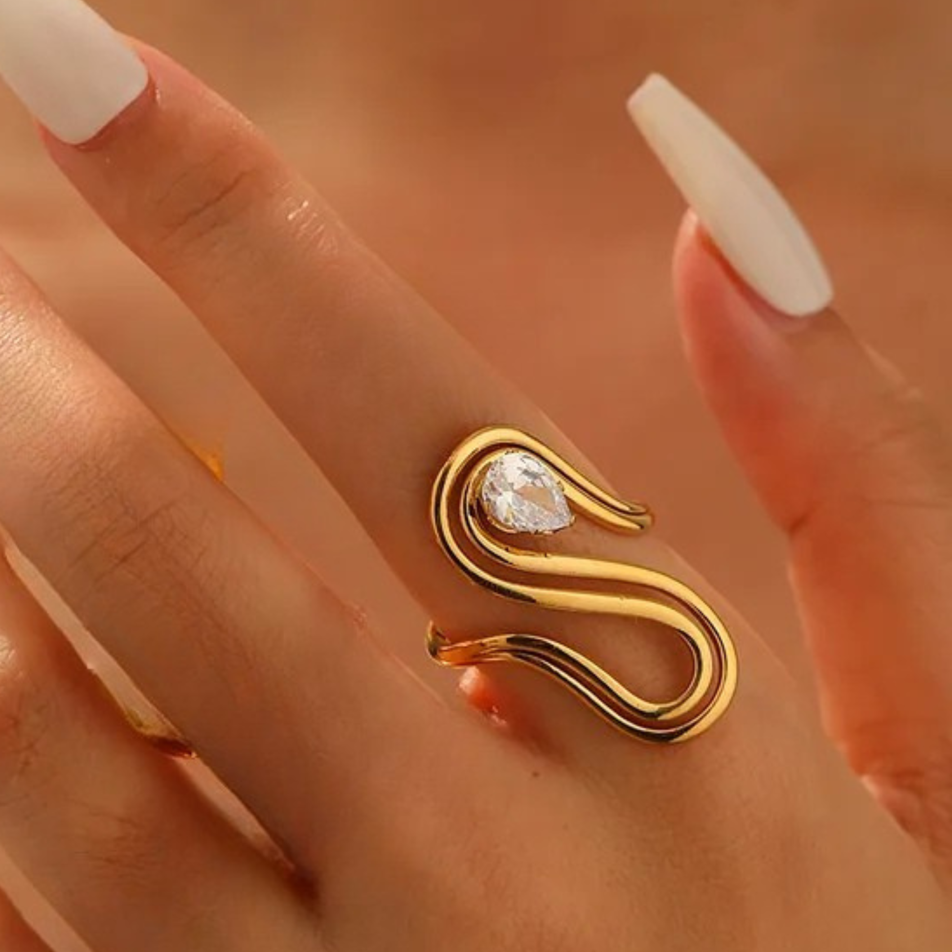 Gold ring with a diamond on a hand with white nail polish against a blurred background
