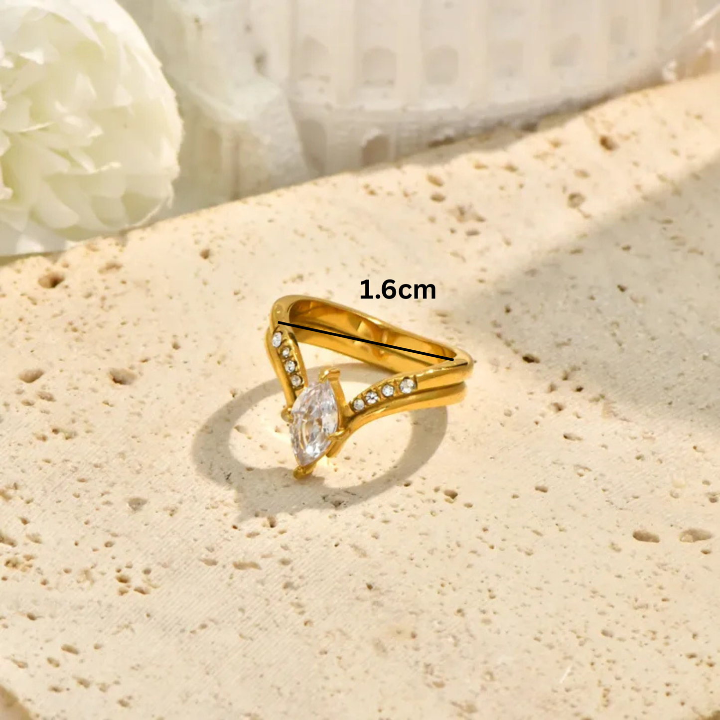 Gold ring with a diamond on a textured beige surface, measurement '1.6cm' displayed.