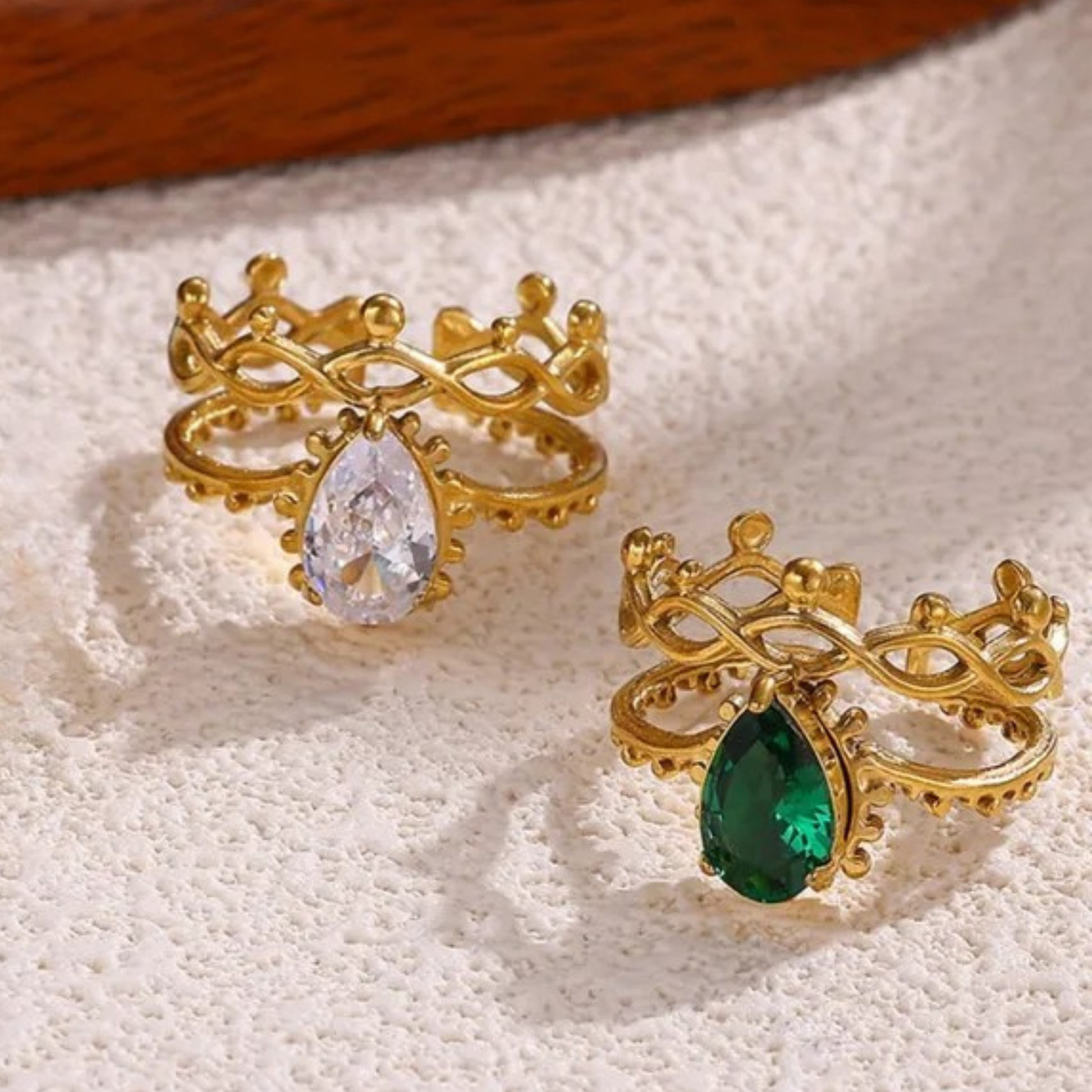 Two gold rings with gemstones on a textured surface
