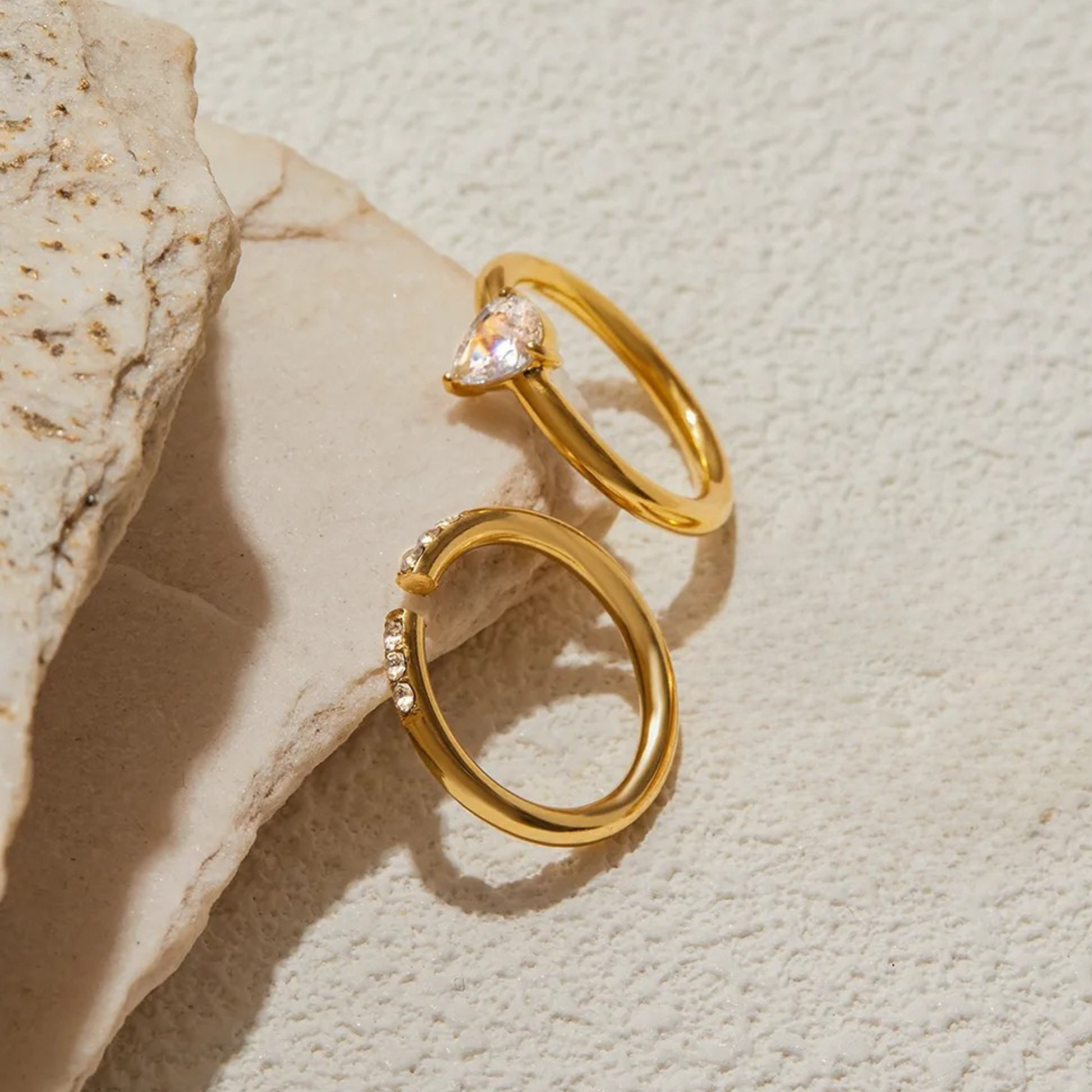 Two gold rings with gemstones on a textured beige surface