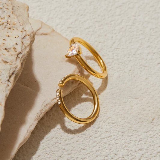 Two gold rings with gemstones on a textured beige surface