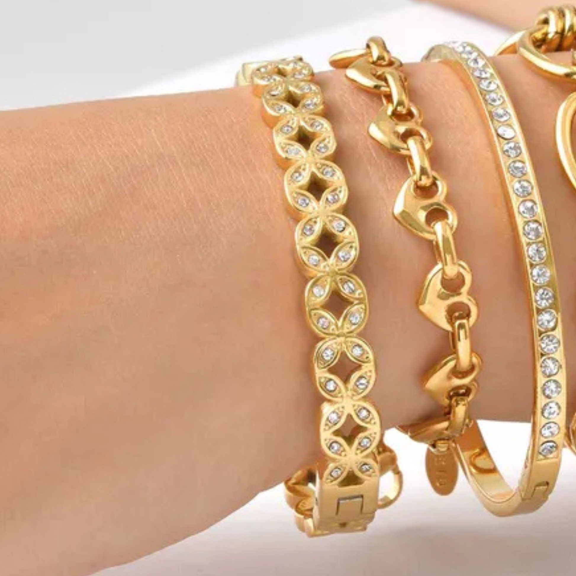Gold bracelets with chain and heart designs on a wrist against a white background