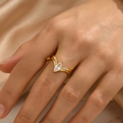 Gold ring with a clear gemstone on a hand against a beige background
