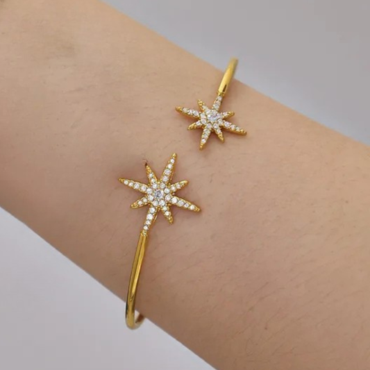 Gold star-shaped earrings on a person's earlobe with a plain background