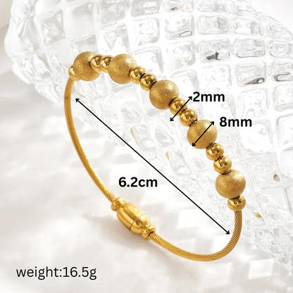 Gold beaded bracelet with measurements on a textured white background