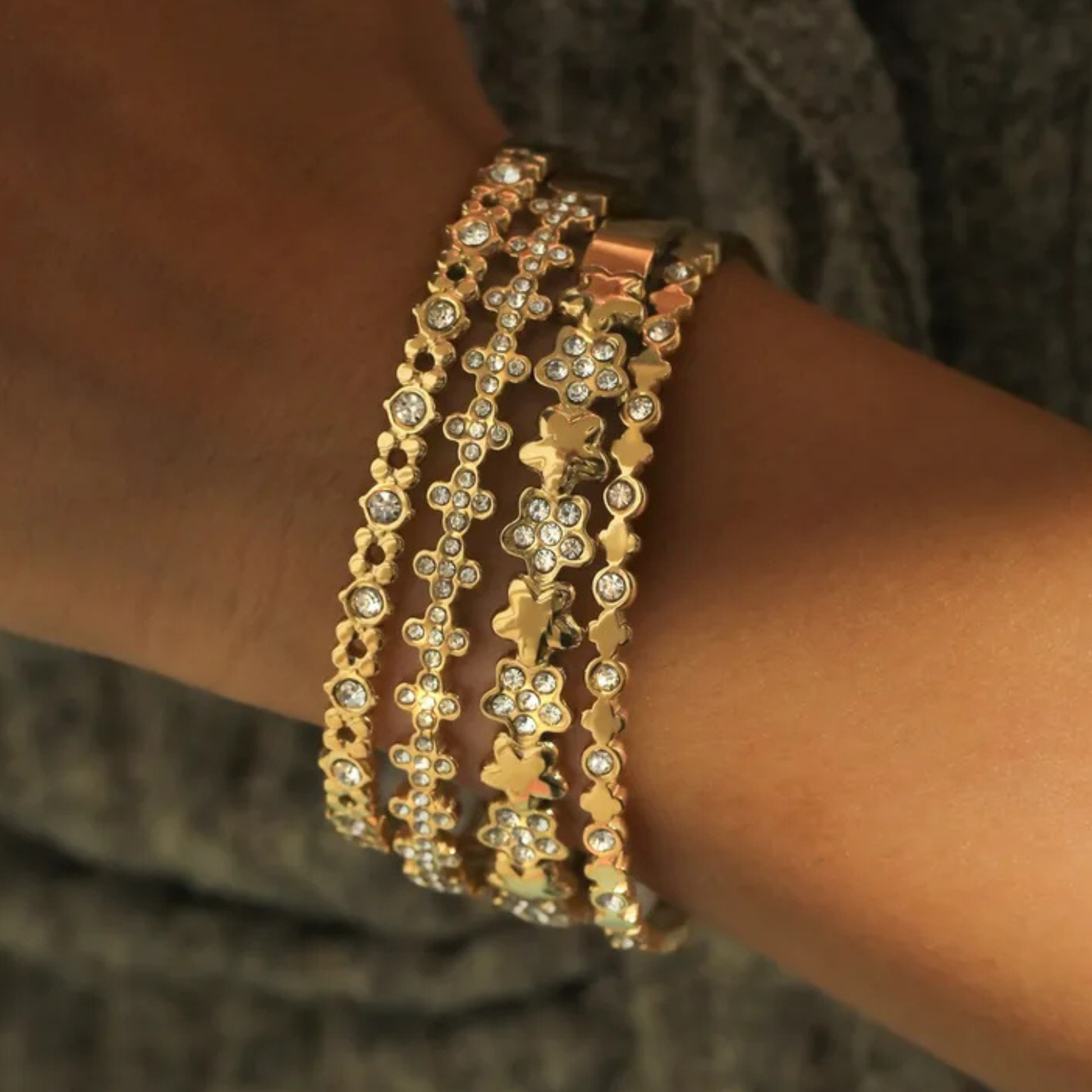 Gold bracelet with floral designs on a wrist against a neutral background
