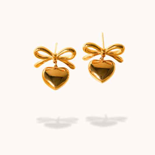 Gold bow and heart shaped earrings on a white background