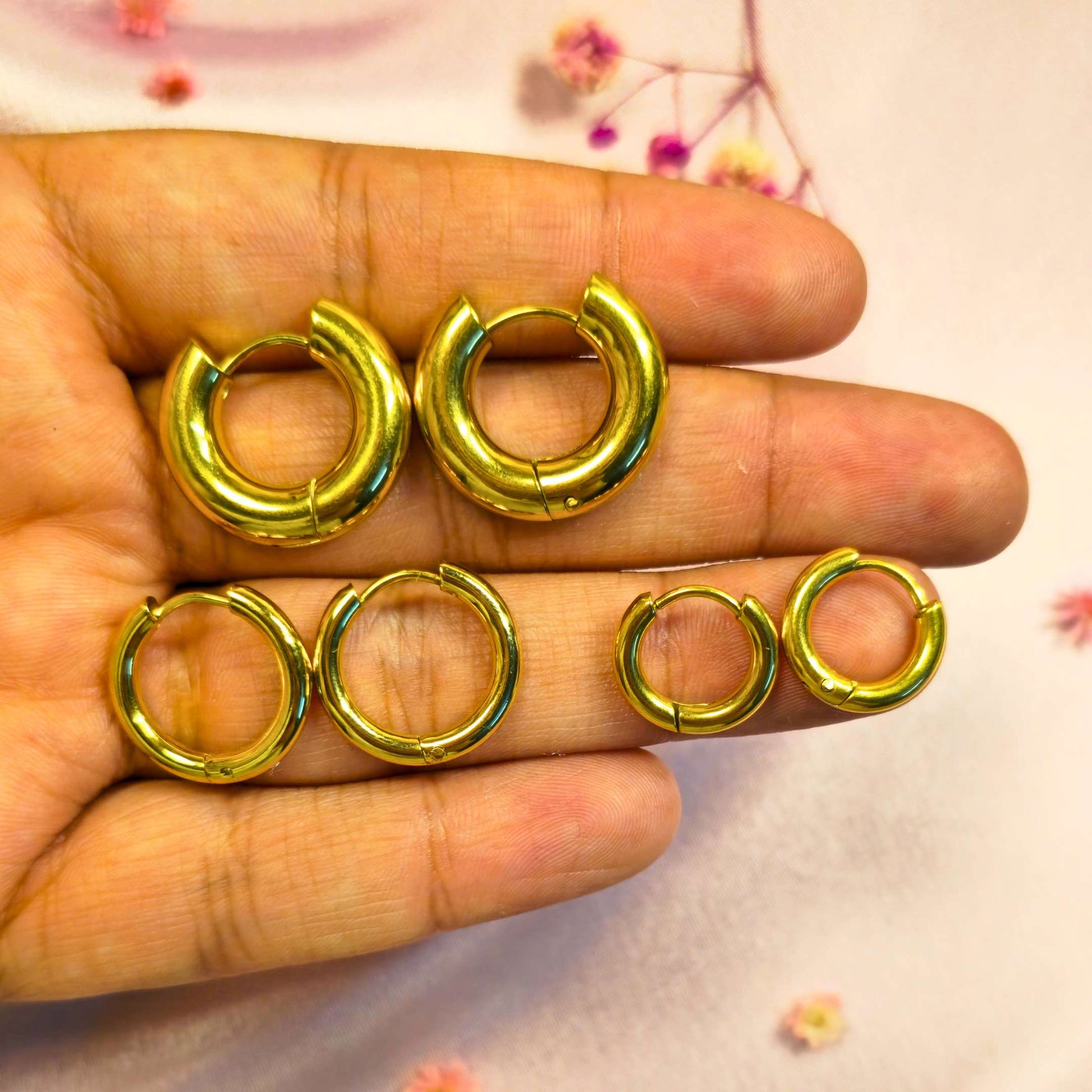 set of Gold hoop earrings held in a hand with a light background